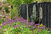 THE MOONGATE GARDEN, SUSSEX: PATH, BORDERS IN SPRING OF ALLIUM FIRMAMENT WITH PURBECK STONE WALL, BLACK PAINTED FENCE, MIRRORS, BOUNDARY, BOUNDARIES, BULBS