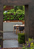 CHELSEA FLOWER SHOW 2018: URBAN FLOW GARDEN, DESIGNER TONY WOODS. VIEW THROUGH PORCELAIN, STEEL EFFECT ARCH TO TABLE, PATIO, LIVING WALL, KITCHEN, DINING AREA, ENTERTAINING