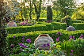 MITTON MANOR, STAFFORDSHIRE:FORMAL PARTERRE. STONE BALL, BOX EDGED BEDS. HEDGES, HEDGING, SPRING, TERRACOTTA CONTAINERS, ALLIUM PURPLE SENSATION,NEIL WILKIN GLASS SCULPTURES