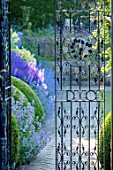 TOWN PLACE GARDEN, SUSSEX: VIEW THROUGH HALF OPENED WROUGHT IRON GATE TO PATH, HERBACEOUS BORDER. SUMMER, ENGLISH, GARDEN, COUNTRY