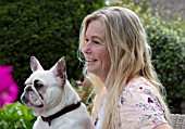 PYTTS HOUSE, OXFORDSHIRE: OWNER ANNA DE KEYSER WITH HER DOG MABLE ON THE TERRACE OUTSIDE THE HOUSE, PATIO, SUMMER. PARASOL