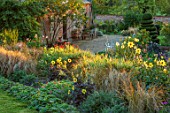 KELMARSH HALL, NORTHAMPTONSHIRE: BORDER WITH DAHLIAS AND GRASSES, GRAVEL PATH BESIDE GLASSHOUSE, CLIPPED TOPIARY TWIST. EVENING LIGHT, ENGLISH, COUNTRY, GARDENS, WALLED