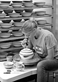 ALHAM FARM, SOMERSET: CORNISHWARE: THE POTTERY - VICKY APPLYING ICONIC BLUE STRIPE BY HAND TO FIRED BOWLS, BLACK AND WHITE