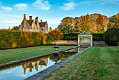 RADCOT HOUSE, OXFORDSHIRE: THE HOUSE SEEN FROM THE LONG POND. BEECH HEDGES, HEDGING, POOL, CANAL, GAZEBO, SEAT, SEATING, AUTUMN, REFLECTIONS, REFLECTED
