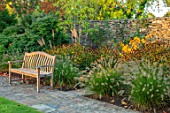 RADCOT HOUSE, OXFORDSHIRE: WOODEN BENCH BESIDE LAWN, HAMAMELIS, PENNISETUM, AUTUMN, BORDERS, FALL, LATE SUMMER, WALLS