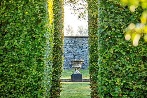 RADCOT_HOUSE_OXFORDSHIRE_VIEW_THROUGH_BEECH_HEDGES_HEDGING_TO_STONE_URN_CONTAINER_IN_LONG_POND
