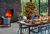 GIBBONS CROFT, WEST CLANDON, SURREY: CHRISTMAS. OPEN PLAN KITCHEN, DINING ROOM. GLASS WALLED EXTENSION, SLATE WALL, FIREPLACE, WOODEN DINING TABLE, CHAIRS, CHRISTMAS TREE