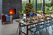 GIBBONS CROFT, WEST CLANDON, SURREY: CHRISTMAS. OPEN PLAN KITCHEN, DINING ROOM. GLASS WALLED EXTENSION, SLATE WALL, FIREPLACE, WOODEN DINING TABLE, CHAIRS, CHRISTMAS TREE