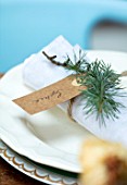 GIBBONS CROFT, WEST CLANDON, SURREY: CHRISTMAS PLACE SETTING ON TABLE. LINEN NAPKIN, FIR SPRIG AND CARDBOARD LUGGAGE LABEL NAME TAG