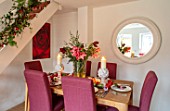 THE CONIFERS, OXFORDSHIRE: CHRISTMAS - KITCHEN DINING ROOM - TABLE, CHAIRS, MIRROR, PRINT OF RED CAMELLIA BY CLIVE NICHOLS, STAIRCASE, VASE WITH AMARYLLIS, PINEAPPLE CANDLES