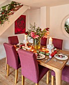 THE CONIFERS, OXFORDSHIRE: CHRISTMAS - KITCHEN DINING ROOM - TABLE, CHAIRS, MIRROR, PRINT OF RED CAMELLIA BY CLIVE NICHOLS, STAIRCASE, VASE WITH AMARYLLIS, PINEAPPLE CANDLES