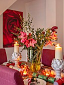 THE CONIFERS, OXFORDSHIRE: CHRISTMAS - KITCHEN DINING ROOM - TABLE, CHAIRS, PRINT OF RED CAMELLIA BY CLIVE NICHOLS, STAIRCASE, VASE WITH AMARYLLIS, PINEAPPLE CANDLES