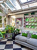 BUTTER WAKEFIELD HOUSE, LONDON: CHRISTMAS - THE GARDEN ROOM. GLASS CONSERVATORY JUST OFF THE KITCHEN WITH SOFA AND BUTTERS CHINA PLATES DISPLAYED ON PLATE RACK. FERNS
