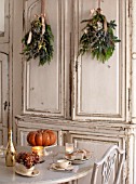 MERRYWOOD, JACKY HOBBS HOUSE, LONDON: WHITE KITCHEN, CHRISTMAS: ORANGE PUMPKINS, TABLE AND CHAIRS, VINTAGE FRENCH CUPBOARDS, PINE AND HYDRANGEA HANGING BOUQUETS