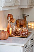 MERRYWOOD, JACKY HOBBS HOUSE, LONDON: WHITE KITCHEN, CHRISTMAS: ORANGE PUMPKINS, CANDLES, TRAY, BRONZE AND GOLD DECORATIONS, CHAMPAGNE, GLASES
