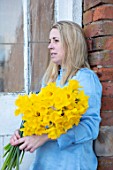 MARBURY HALL, SHROPSHIRE: DESIGNER SOFIE PATON-SMITH, SOFIE WITH BUNCH OF DAFFODILS IN FRONT OF GREENHOUSE, SPRING