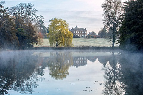THENFORD_GARDENS__ARBORETUM_NORTHAMPTONSHIRE_THE_LAKE_AND_HOUSE_WITH_WILLOW_TREE_MORNING_MIST_SPRING