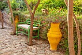 TAROUDANT, MOROCCO: DESIGNERS ARNAUD MAURIERES AND ERIC OSSART: SUNKEN PATIO, PAVING, GREEN BENCHES, SEATS, ACACIA TREES, SHADE, SHADY, YELLOW, TERRACOTTA, CONTAINERS