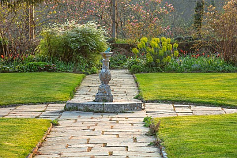 GRAVETYE_MANOR_SUSSEX_SPRING_APRIL_COUNTRY_GARDEN_LUTYENS_BENCH_SEAT_ON_LAWN_PATHS_AND_STONE_SUNDIAL