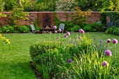 DESIGNER JAMES SCOTT, THE GARDEN COMPANY: LAWN, MEADOW SQUARE WITH ALLIUM VIOLET BEAUTY, LAWN,  WOODEN CHAIRS, WALL, RUSTY METAL WALL ORNAMAMENT, MAY, SPRING