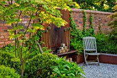 DESIGNER JAMES SCOTT, THE GARDEN COMPANY: BARBEQUE, WOODEN CHAIRS, WALL, RUSTY METAL WALL ORNAMAMENT, MAY, SPRING, ALLIUMS, GRAVEL