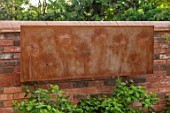 DESIGNER JAMES SCOTT, THE GARDEN COMPANY: WALL WITH CORTEN STEEL WALL PLAQUE WITH CUT OUT ALLIUMS. ORNAMENT, METAL