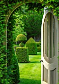 WINSON MANOR, GLOUCESTERSHIRE: VIEW THROUGH WOODEN GATE TO LAWN AND TOPIARY, CLIPPED, YEW, TAXUS, GREEN, GARDEN, SUMMER, ENGLISH, COUNTRY
