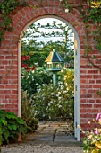 MANOR FARM, CHESHIRE: VIEW THROUGH GATE, BRICK ARCH TO BIRDFEEDER AND, TERRACE WITH CISTUS CYPRIUS, FOCAL POINT, ENGLISH, COUNTR, GARDEN, SUMMER