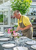 CLAUS DALBY GARDEN, DENMARK: CLAUS PUTTING VASES OF ROSES ON OUTDOOR TABLE
