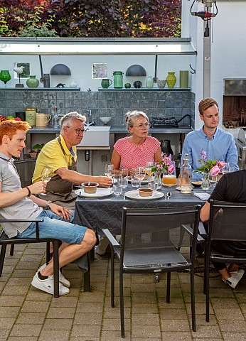 CLAUS_DALBY_GARDEN_DENMARK_CLAUS_AND_FRIENDS_EATING_AT_A_TABLE_ON_PATIO_OUTDOOR_KITCHEN
