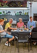 CLAUS DALBY GARDEN, DENMARK: CLAUS AND FRIENDS EATING AT A TABLE ON PATIO, OUTDOOR KITCHEN