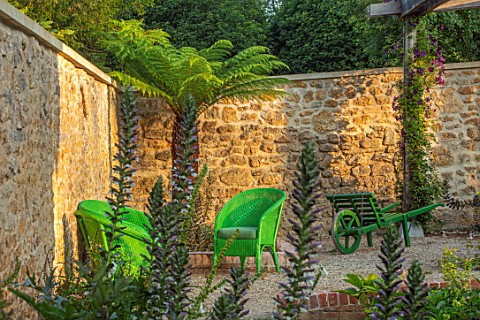 THE_NEWT_IN_SOMERSET_CORNER_OF_COTTAGE_GARDEN_IN_JULY_ACANTHUS_MOLLIS_PALM_GREEN_WICKER_SEATS_SEATIN
