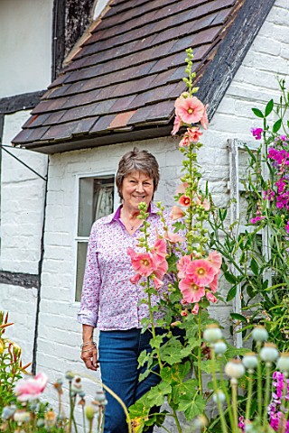 THATCH_COTTAGE_WORCESTERSHIRE_OWNER_MARY_COX_SURROUNDED_BY_TALL_HOLLYHOCKS