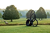 ROCKCLIFFE GARDEN, GLOUCESTERSHIRE: VIEW ACROSS LAWN AT SUNRISE WITH BORROWED LANDSCAPE, BRONZE SCULPTURE SOUTHERN SHADE BY NIGEL HALL