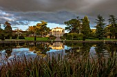 THORP PERROW ARBORETUM, YORKSHIRE: THE VIEW OF THE HOUSE ACROSS THE LAKE IN AUTUMN. TREES, LAKES, WATER, EVENING LIGHT, REFLECTIONS, REFLECTED