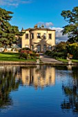 THORP PERROW ARBORETUM, YORKSHIRE: HOUSE ACROSS THE LAKE IN AUTUMN. TREES, LAKES, WATER, EVENING LIGHT, REFLECTIONS, REFLECTED