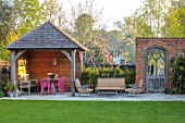 LITTLE ORCHARDS, SURREY, DESIGNER NIC HOWARD: SHED, OUTBUILDING, TABLE, PINK CHAIRS, PERGOLA, SEATING AREA, WALL, GOTHIC DOOR, DOORWAY, LAWN