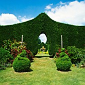 ARCHWAY IN SHAPED LEYLANDII HEDGE WITH TOPIARY IN FOREGROUND.  STOURTON HOUSE  WILTSHIRE