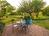 SILVER STREET FARM, DEVON. DESIGNER ALASDAIR CAMERON - PATIO, TERRACE, SUNSET, EVENING, TABLE, CHAIRS, FLOWERS, COPPER, CONTAINER, HERBS, SPRING, MAY