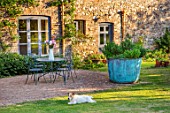 SILVER STREET FARM, DEVON. DESIGNER ALASDAIR CAMERON - PATIO, TERRACE, SUNSET, EVENING, TABLE, CHAIRS, FLOWERS, COPPER, CONTAINER, HERBS, SPRING, MAY, DOG, PET