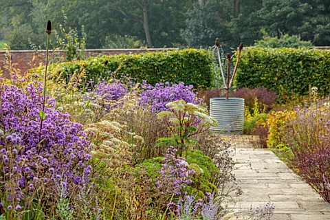 WILDEGOOSE_NURSERY_SHROPSHIRE_DOUBLE_BORDERS_IN_SEPTEMBER_PATHS_METAL_CONTAINER_WITH_SCULPTURE_ASTER