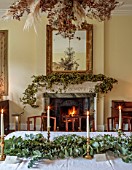 MARBURY HALL, SHROPSHIRE: DESIGNER SOFIE PATON-SMITH - DINING ROOM, FIREPLACE GARLAND OF HOPS, TABLE, CHAIRS, EUCALYPTUS TABLE DECORATION, CANDLES, DECEMBER