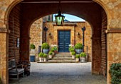 PRIORS MARSTON, WARWICKSHIRE: VIEW THROUGH ARCHWAY, FRONT DOOR, STEPS, TERRACOTTA CONTAINERS, CLIPPED TOPIARY BOX, BUXUS, WHITE FLOWERS OF TULIP, TULIPA WHITE TRIUMPHATOR, SPRING