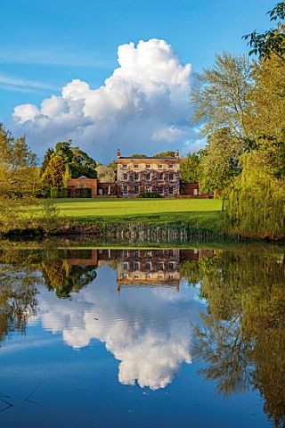 PRIORS_MARSTON_WARWICKSHIRE_VIEW_ACROSS_LAKE_POND_WATER_TO_HOUSE_SPRING_MAY_HOUSE_REFLECTIONS_REFLEC
