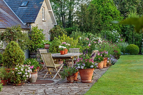 WESTBROOK_HOUSE_SOMERSET_TERRACE_PATIO_LAWN_WOODEN_TABLE_CHAIRS_TERRACOTTA_CONTAINERS_GERANIUMS_COUN