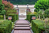THE LASKETT GARDENS, HEREFORDSHIRE. DESIGNER ROY STRONG: VIEW ALONG PATH TO COLONNADE COURT, HEDGES, HEDGING, STEPS, FINIALS, JULY, SUMMER, WOODEN, SEATS, BENCHES