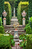 THE LASKETT GARDENS, HEREFORDSHIRE. DESIGNER ROY STRONG - THE SILVER JUBILEE GARDEN, SUNDIAL, BRICK PATH, URNS, CONTAINERS, TULIPS, BOX HEDGING, HEDGES, SPRING, APRIL