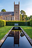 STOCKCROSS HOUSE, BERKSHIRE: LONG NARROW BLACK POOL WITH CHURCH REFLECTED IN IT, WOODEN BENCH, LAWN, HEDGES, REFLECTIONS