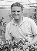 PRIMROSE HALL PEONIES, BEDFORDSHIRE: BLACK AND WHITE PHOTOGRAPH OF NURSERY OWNER ALEC WHITE IN A GLASSHOUSE WITH ALSTROEMERIA FLOWERS, SUMMER