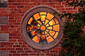MORTON HALL, WORCESTERSHIRE: WEST GARDEN, SUNSET, ROUND WINDOW ON WALL WITH SUNSET REFLECTED IN GLASS
